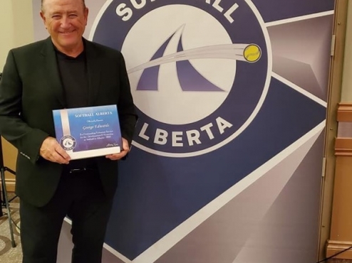 George Edwards holds his Merit Award in front of a Softball Alberta sign